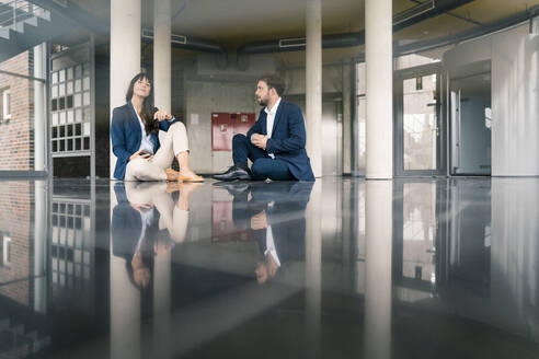 Professional male and female colleagues discussing while sitting in lobby at office  - JOSEF02559