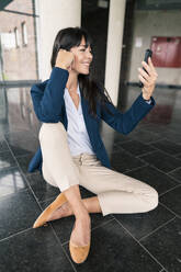 Female entrepreneur taking selfie on smart phone in lobby - JOSEF02566