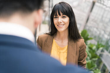 Mature businesswoman smiling while looking at male colleague during office meeting - JOSEF02594