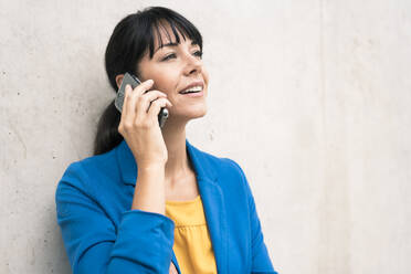 Reife Geschäftsfrau, die mit ihrem Smartphone an der Wand im Büro spricht - JOSEF02596