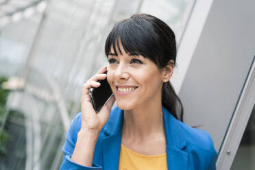 Lächelnde Geschäftsfrau, die im Büro mit einem Mobiltelefon spricht - JOSEF02600