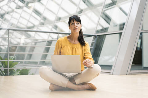 Businesswoman with laptop sitting on floor in office corridor stock photo