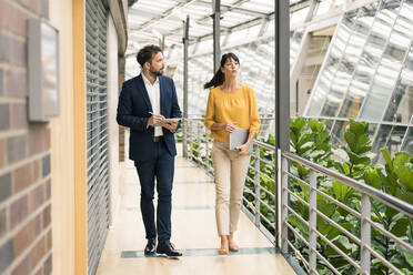 Male entrepreneur discussing while walking with female colleague in office corridor - JOSEF02617