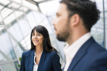 Smiling businesswoman standing by male colleague looking away in office during meeting - JOSEF02629