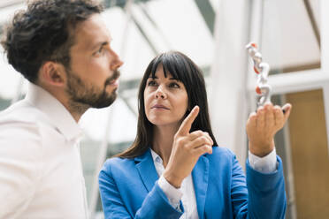 Businessman analyzing model standing by female colleague in office - JOSEF02635