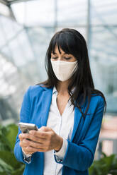 Female entrepreneur text messaging on mobile phone in office during pandemic - JOSEF02638