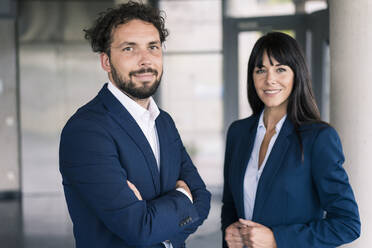 Male colleague with arms crossed by female entrepreneur in lobby - JOSEF02644