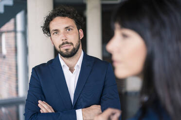 Male entrepreneur with arms crossed by female colleague in lobby - JOSEF02646