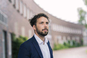 Male professional looking away outside building in office park - JOSEF02655