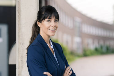 Smiling female entrepreneur by column at office park  - JOSEF02668