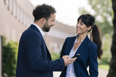 Smiling colleagues with smart phone at office park - JOSEF02673