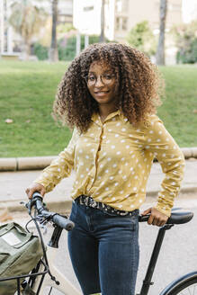 Lockenköpfige Frau mit Fahrrad auf der Straße stehend - XLGF00788