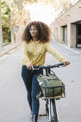Woman looking away while walking with bicycle on road - XLGF00791