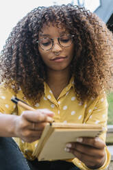 Young woman writing in book while sitting outdoors - XLGF00797