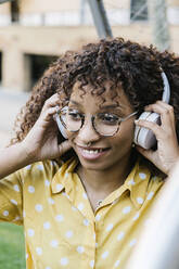 Smiling woman wearing headphones listening music while standing outdoors - XLGF00808