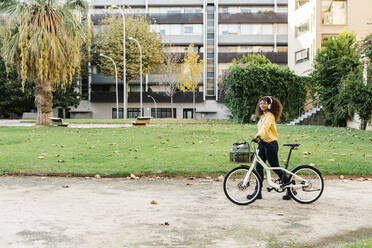 Woman wearing headphones listening music while walking with bicycle on footpath - XLGF00811