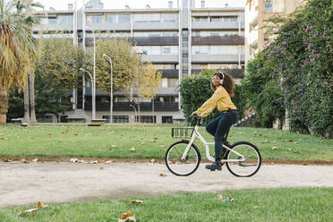 Young woman listening music while riding bicycle on footpath - XLGF00814