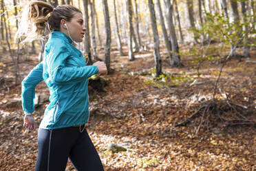 Sportlerin mit In-Ear-Kopfhörern hört Musik beim Laufen im Wald - JSRF01252