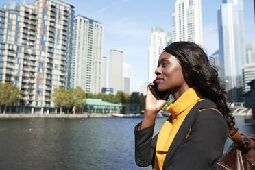 Weibliche Fachkraft beim Telefonieren vor einem Fluss an einem sonnigen Tag - PMF01625