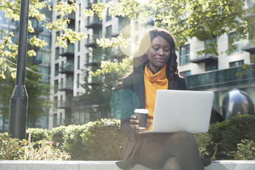 Smiling businesswoman having coffee while working on laptop at office park - PMF01627