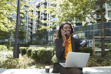 Lächelnde Geschäftsfrau mit Laptop im Gespräch am Telefon im Büropark - PMF01628