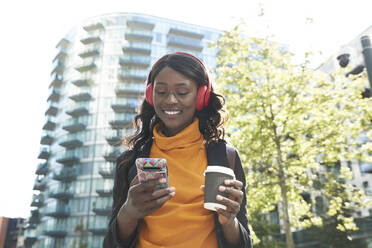 Smiling female professional with disposable coffee cup listening music at office park - PMF01640