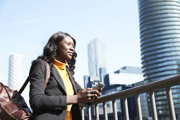 Smiling businesswoman looking away while standing by railing on sunny day - PMF01650