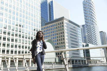 Smiling businesswoman talking on call while walking by railing on sunny day - PMF01656