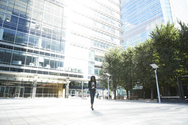 Businesswoman using mobile phone while walking in city on sunny day - PMF01665