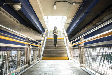 Geschäftsfrau, die ein Mobiltelefon benutzt, während sie auf einer Treppe in einer U-Bahn-Station geht - PMF01686