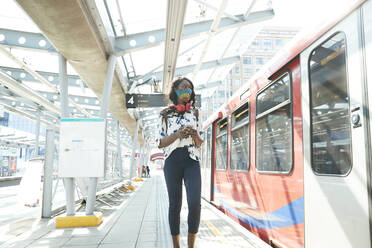 Businesswoman wearing face mask using mobile phone while standing at station platform - PMF01687