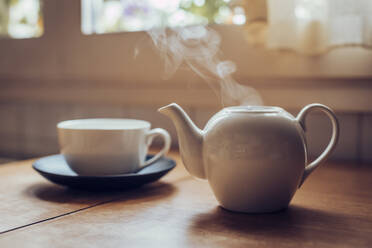 Crop view of female holding porcelain teapot and pouring hot tea into red  ceramic polka-dotted?