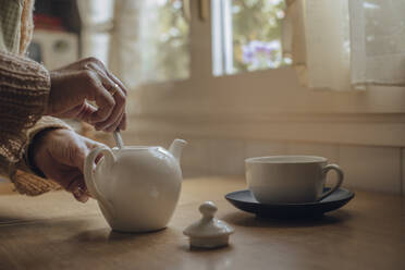 Ältere Frau bereitet mit ihren Händen Tee im Kessel auf dem Küchentisch zu - ACPF00966