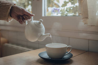 Crop view of female holding porcelain teapot and pouring hot tea into red  ceramic polka-dotted?