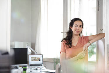 Smiling businesswoman leaning on door in office cabin - FKF03884