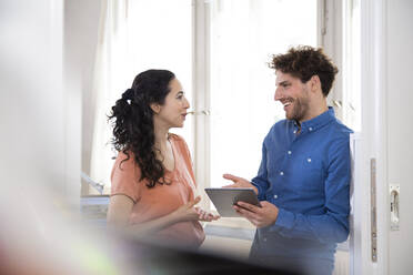 Happy male professional talking with female colleague while holding digital tablet in office meeting - FKF03888