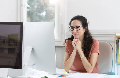 Smiling businesswoman with hand on chin working in office cabin - FKF03920