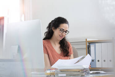 Smiling businesswoman reading document while working in office cabin - FKF03923