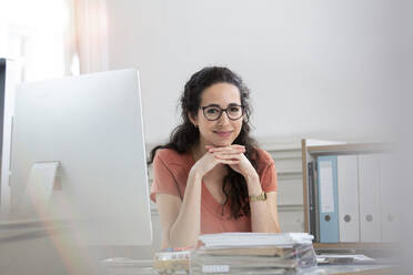 Smiling businesswoman with hand on chin sitting in office - FKF03925