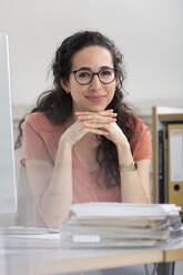 Businesswoman smiling with hand on chin sitting in office - FKF03929