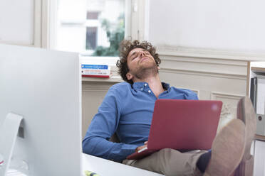 Young businessman sleeping with laptop in office cabin - FKF03938