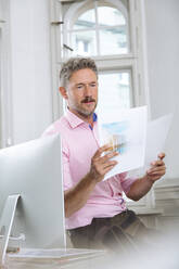 Männliche Fachkraft liest Papierdokument am Computer im Büro - FKF03944