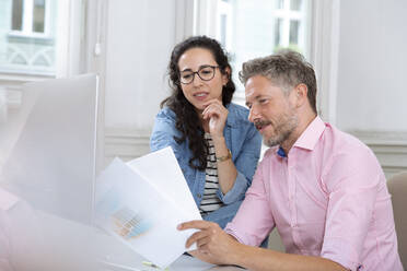 Female and male professionals discussing over document in meeting at office - FKF03945