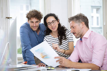 Female professional with male colleagues discussing over document in office meeting - FKF03948