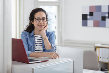 Weibliche Fachkraft sitzt am Laptop am Schreibtisch im Büro - FKF03950