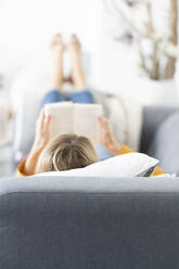 Blonde Frau liest ein Buch und entspannt sich auf dem Sofa zu Hause - CHPF00731