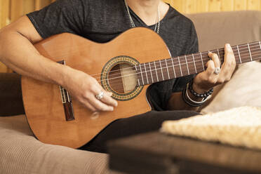Mann spielt Akustikgitarre, während er zu Hause sitzt - LJF01873
