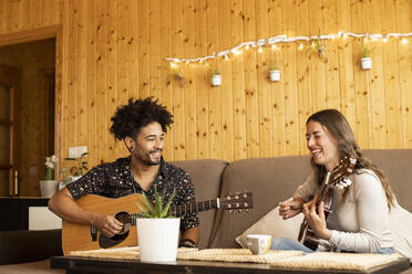Freundin lächelnd beim Gitarrenspielen neben ihrem Freund zu Hause sitzend - LJF01877