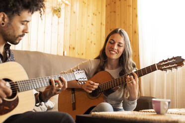 Lächelnde Frau spielt Gitarre und sitzt neben einem Mann zu Hause - LJF01880