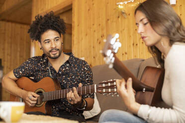 Couple rehearsing with guitar together while sitting at home - LJF01881